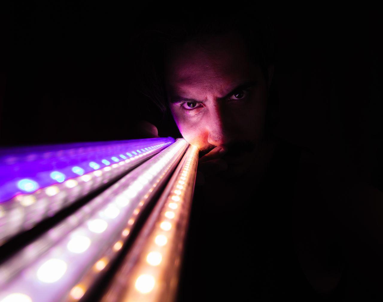 Striking close-up of a man with intense gaze illuminated by vibrant LED lights.