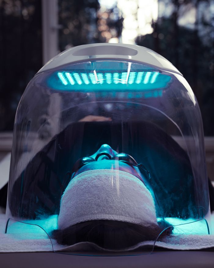 about-02 Person receiving LED light therapy under blue light dome for advanced skincare treatment.
